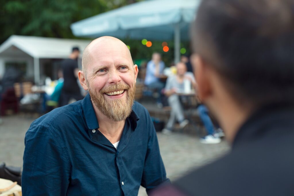 smiling man talking to friend at sidewalk cafe